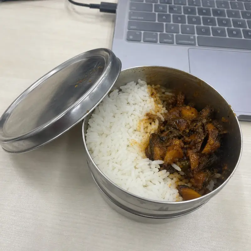 An open steel tiffin box of rice and masala on a desk
