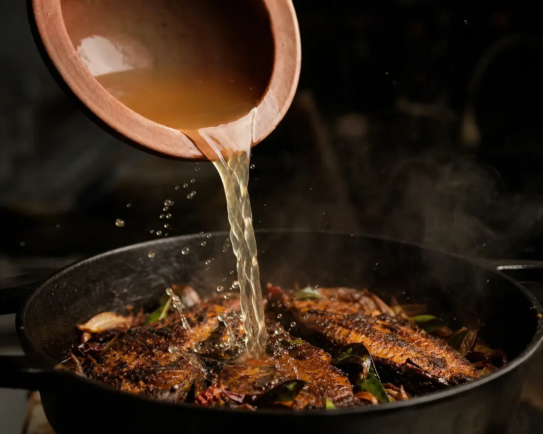 Coconut vinegar poured into a hot pan of spiced fish